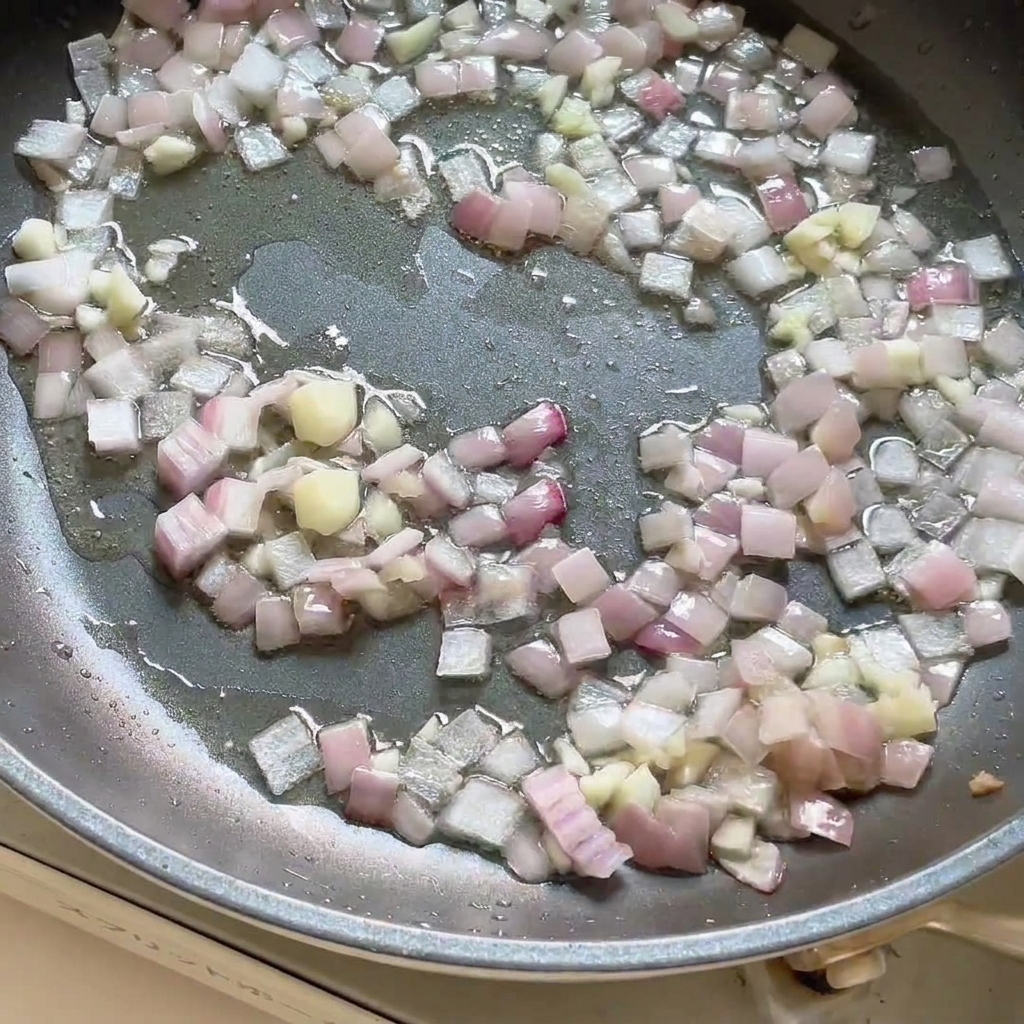 Pasta de curry añadida a la sartén que contiene las cebollas y el ajo salteados, mezclándose todo.