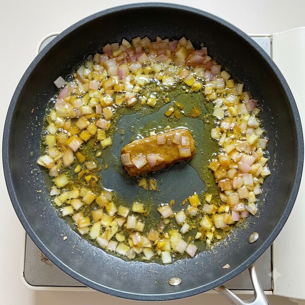 Agua y leche de coco vertidas en la base de curry en una sartén, removidas hasta obtener una consistencia espesa.