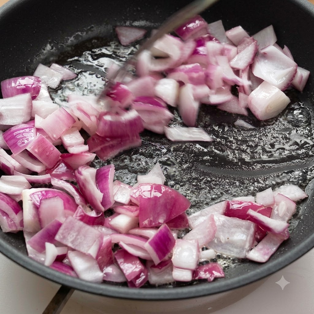 Cebollas moradas picadas siendo salteadas en aceite dentro de una sartén.