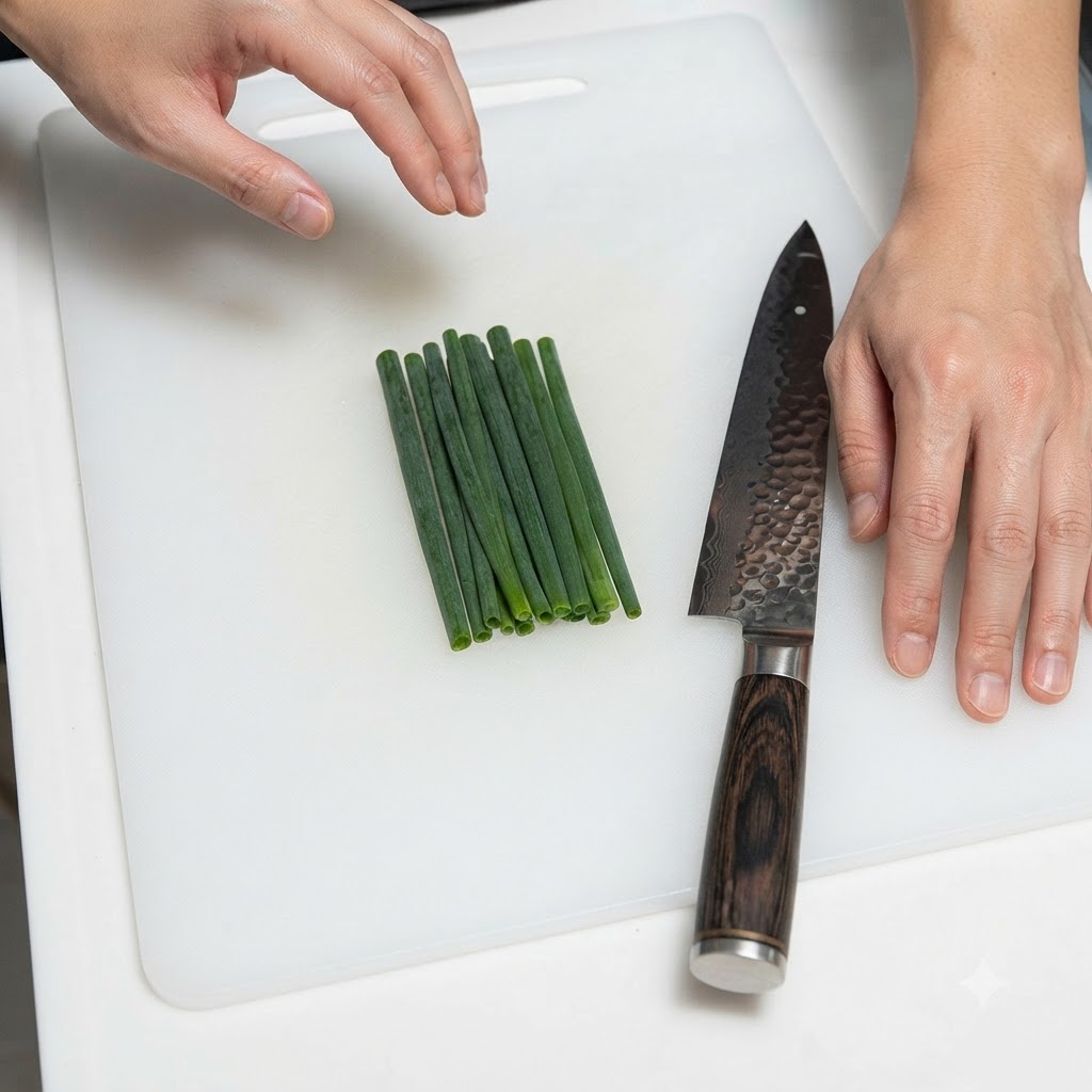 Un manojo de cebollines ordenados cuidadosamente junto a un cuchillo de cocina en una tabla de cortar blanca.