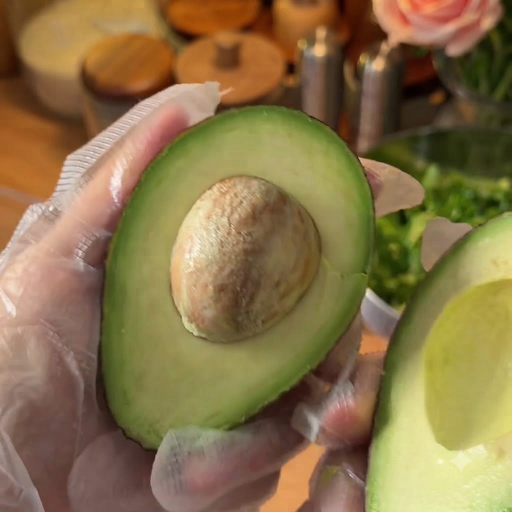 Un aguacate fresco partido por la mitad siendo preparado en una tabla de cortar.