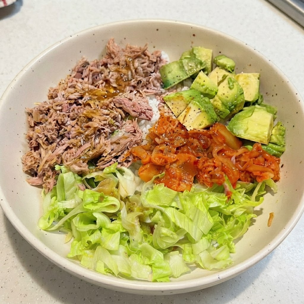 Un bol de arroz con atún y aguacate ensamblado con el aderezo rociado sobre los ingredientes superiores.