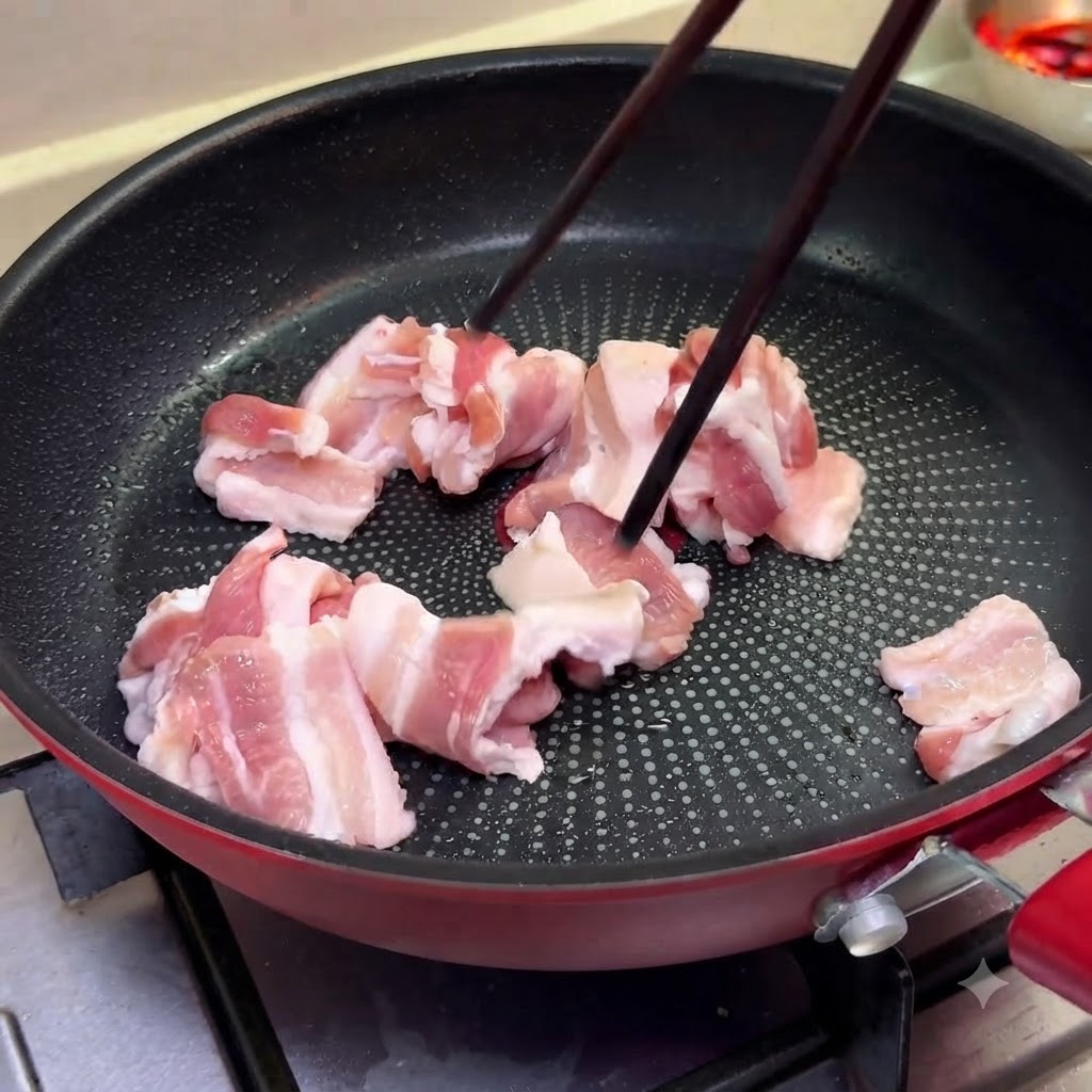 Rodajas finas de panceta de cerdo cocinándose en una sartén a fuego medio usando palillos.