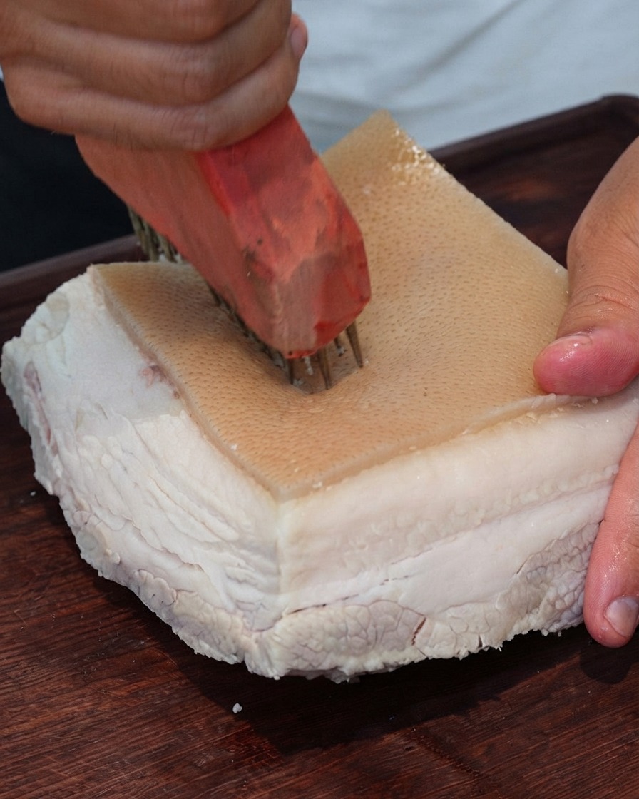 Primer plano de una herramienta para pinchar carne haciendo agujeros repetidamente en la superficie de la piel de cerdo.