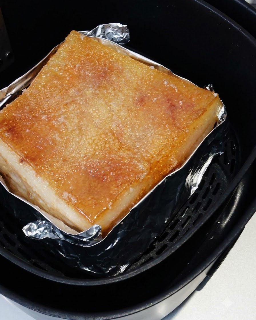 La panceta de cerdo asada dentro de la cesta de la air fryer con su piel salada cocinada a un tono dorado.