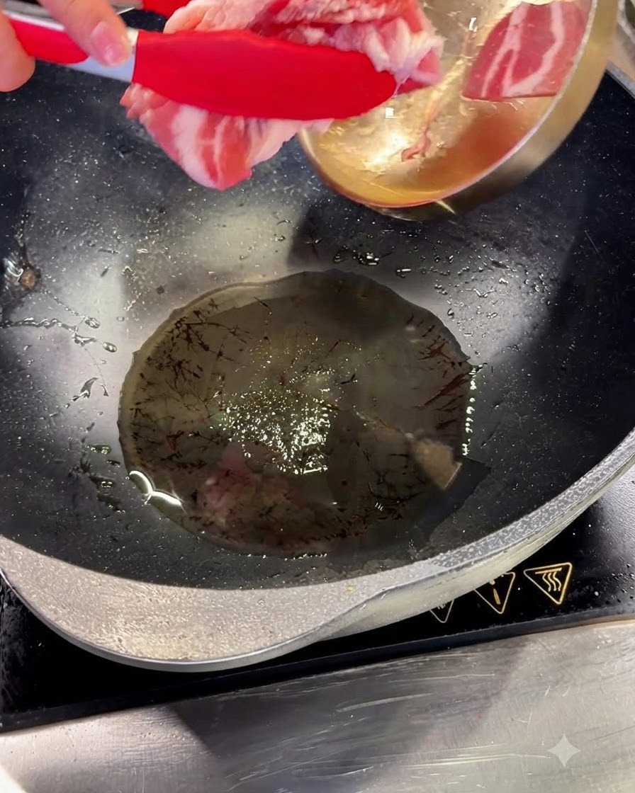 Rodajas de panceta de cerdo siendo añadidas a aceite caliente en un wok usando pinzas rojas.