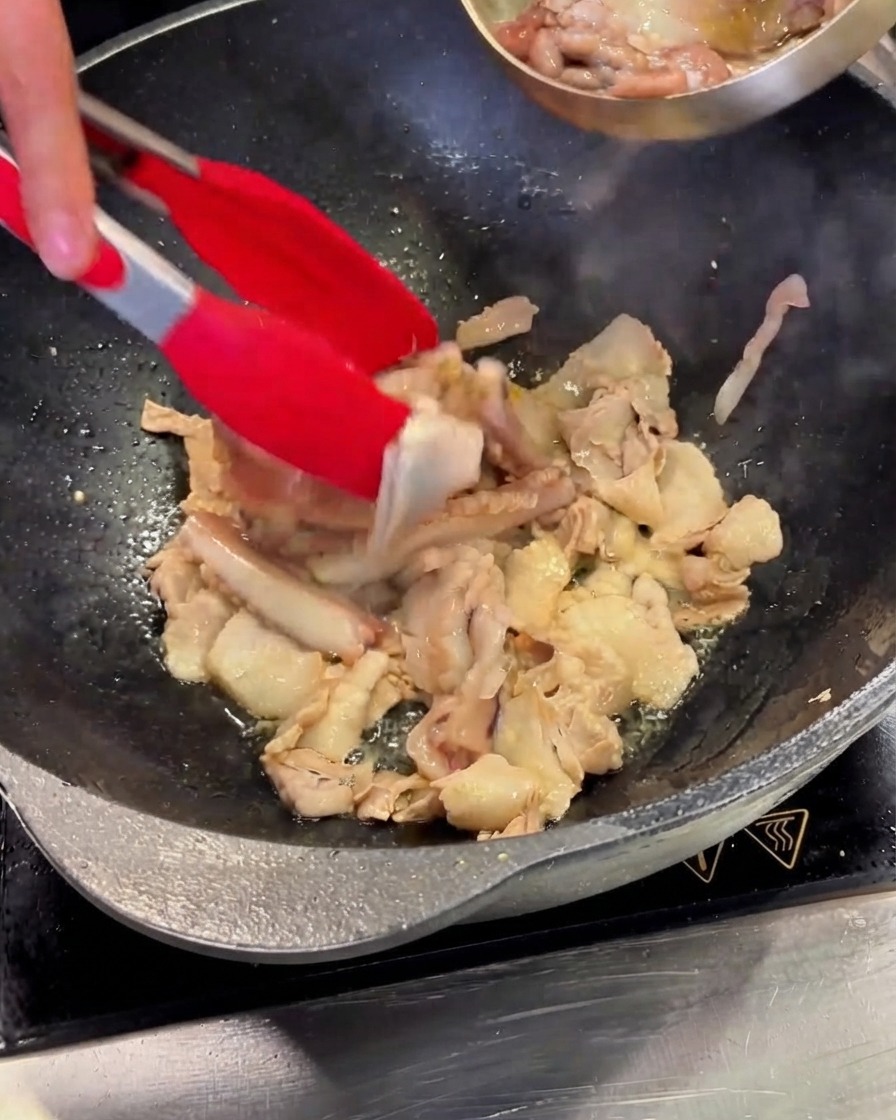 Trozo de calamar limpio siendo vertido desde un tazón de acero hacia el wok que contiene la panceta.