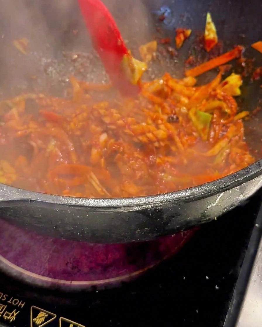 Una espátula roja removiendo la mezcla chisporroteante en el wok bajo fuego fuerte.