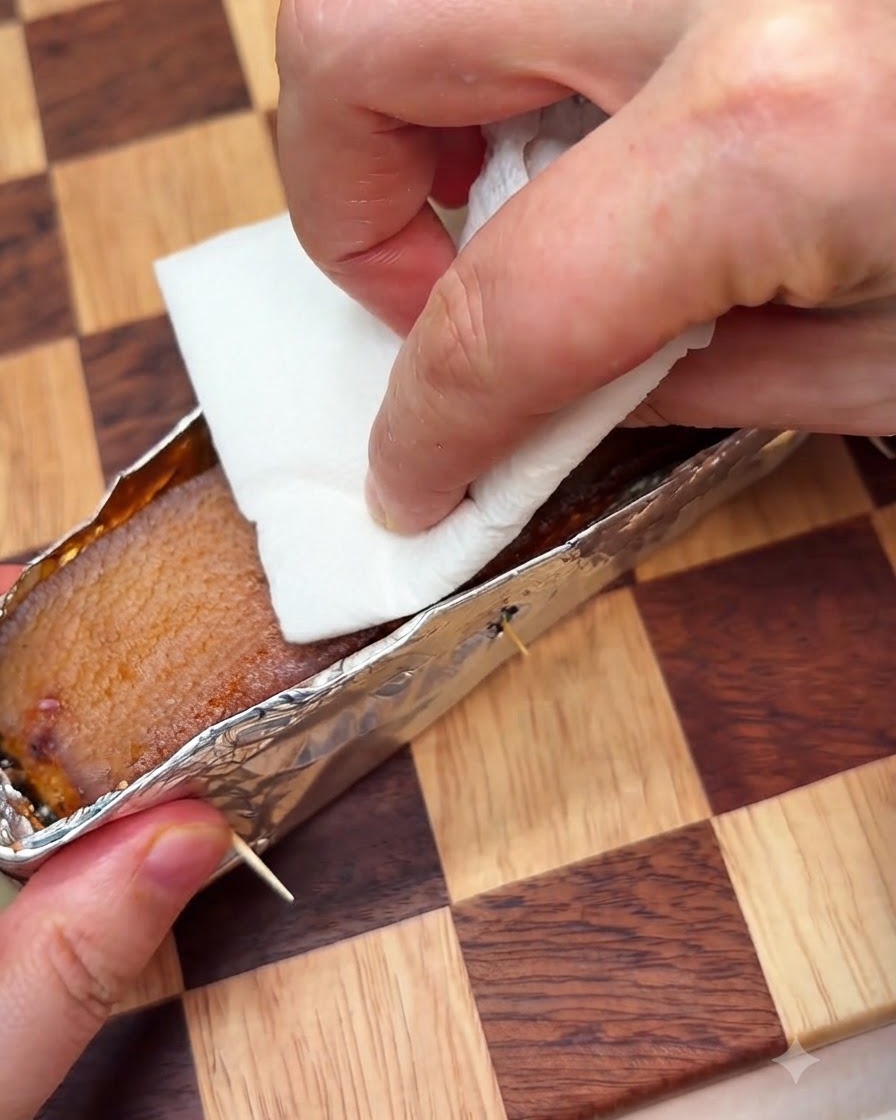 Una toalla de papel siendo presionada sobre la piel del cerdo dentro de una bandeja de aluminio mientras se perfora.
