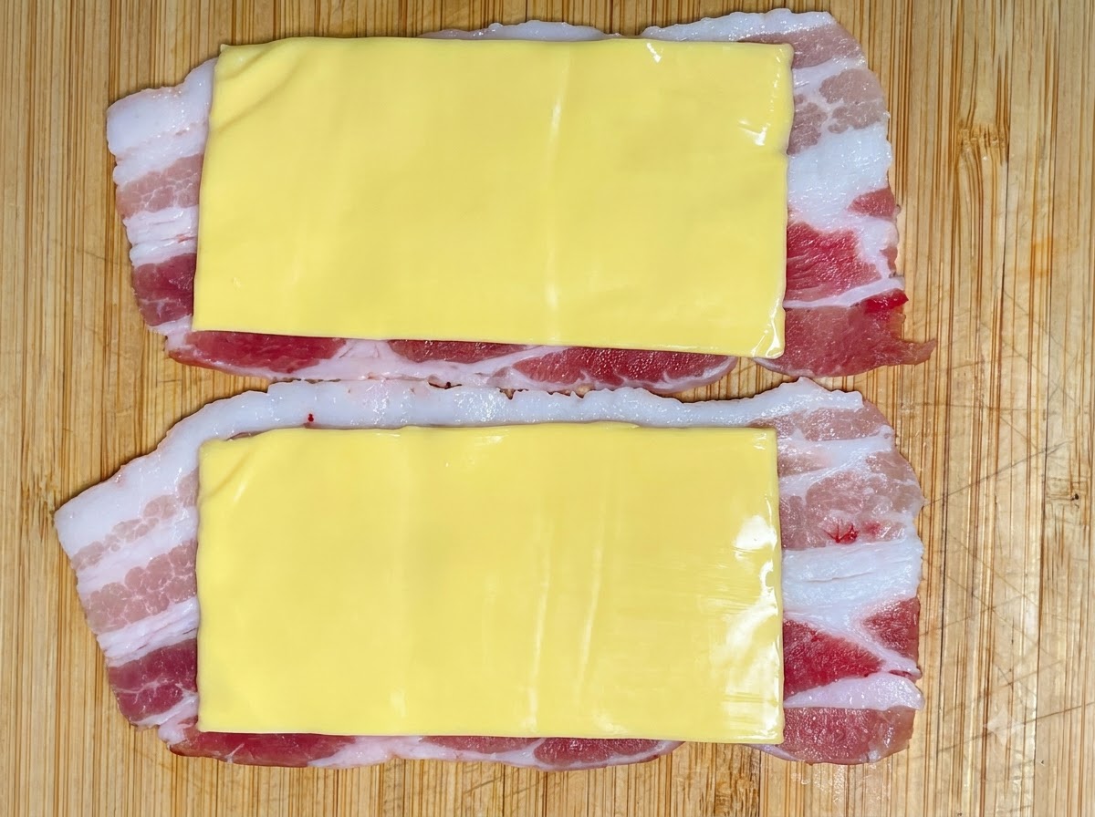 Pasta de camarones siendo exprimida desde una manga pastelera sobre las capas de cerdo y queso.