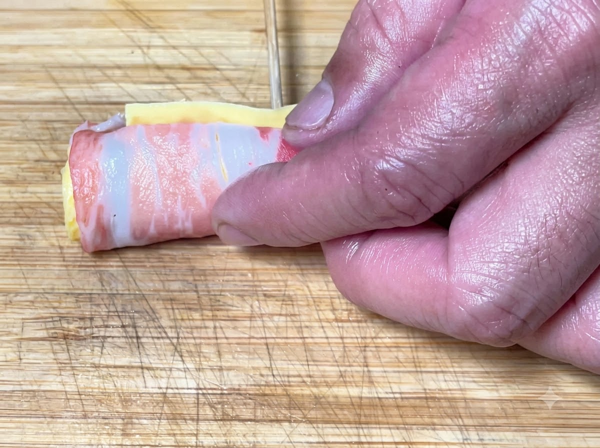 Manos enrollando las capas de panceta y asegurando la forma de cilindro con brochetas de bambú.