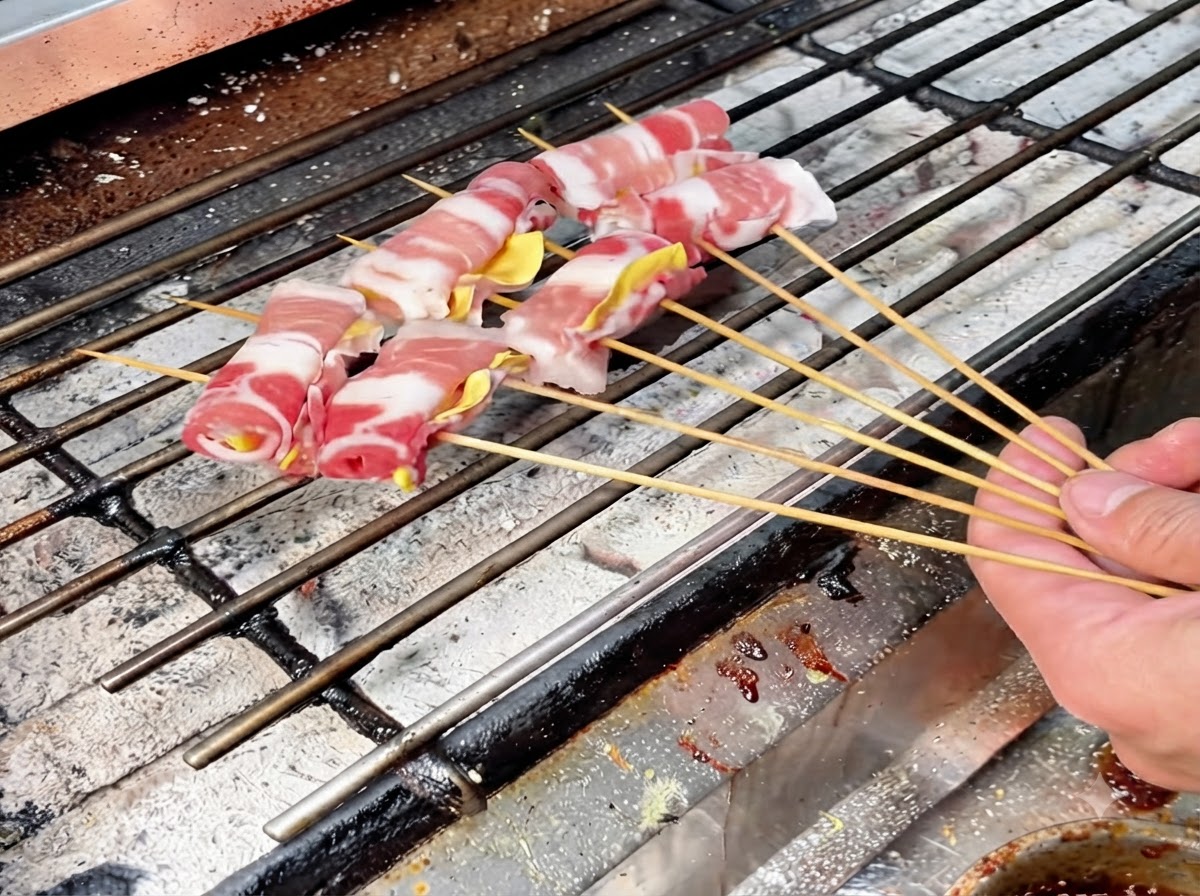 Varios rollitos de carne ensartados y dispuestos sobre una parrilla de carbón caliente para un asado lento.