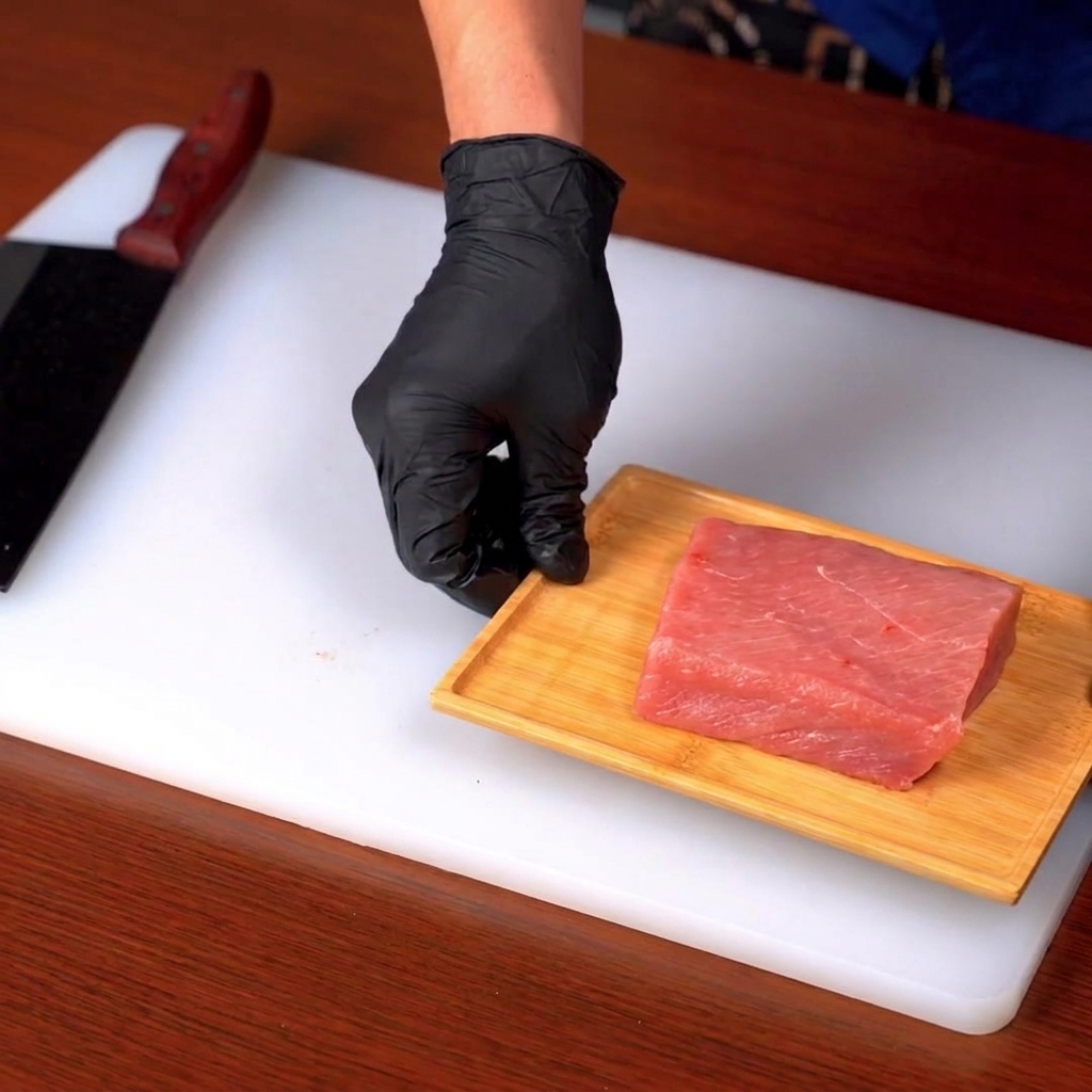 Un corte de lomo de cerdo crudo siendo cortado en una tabla de madera sobre una superficie blanca.