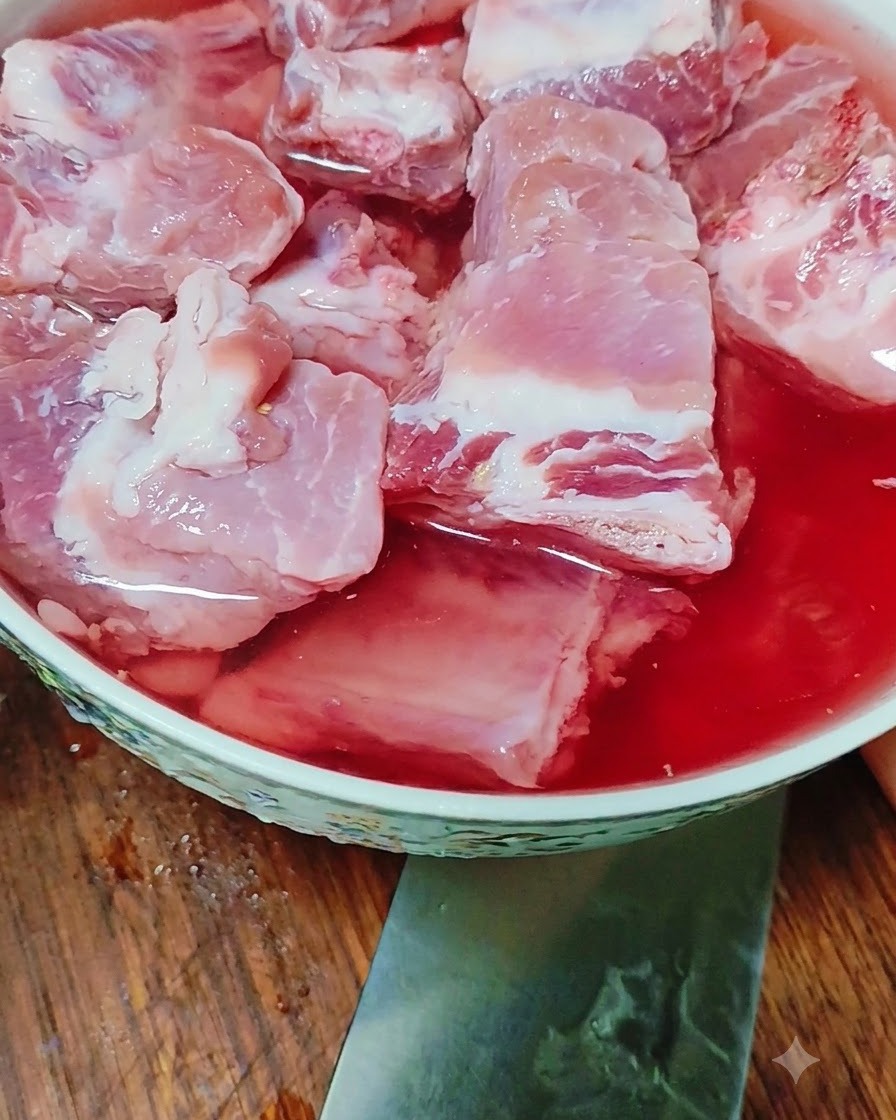 Costillas de cerdo crudas remojándose en un bol lleno de agua teñida de rojo.