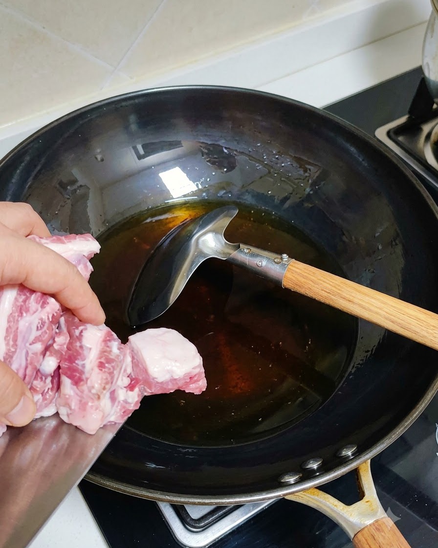 Costillas de cerdo escaldadas añadiéndose a un wok caliente con aceite.