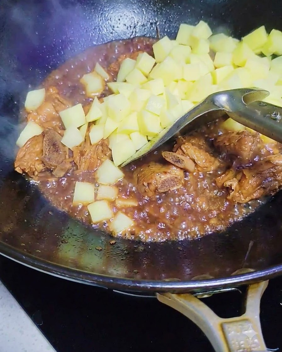 Patatas crudas en cubos añadiéndose al wok con las costillas de cerdo y la salsa.