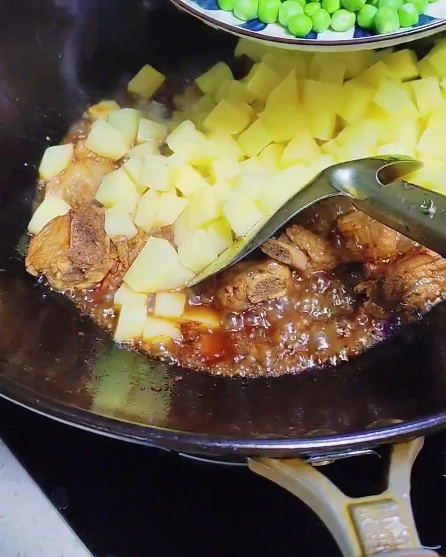 Guisantes verdes y rodajas de salchicha añadiéndose al wok con las costillas de cerdo y patatas burbujeantes.