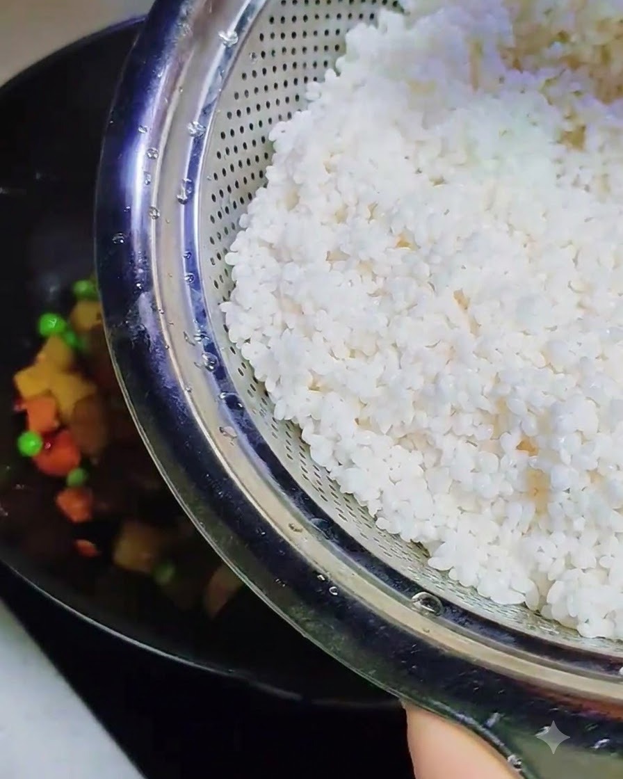 Arroz glutinoso remojado y suave vertiéndose desde un colador de metal hacia el wok que contiene los demás ingredientes cocinados.