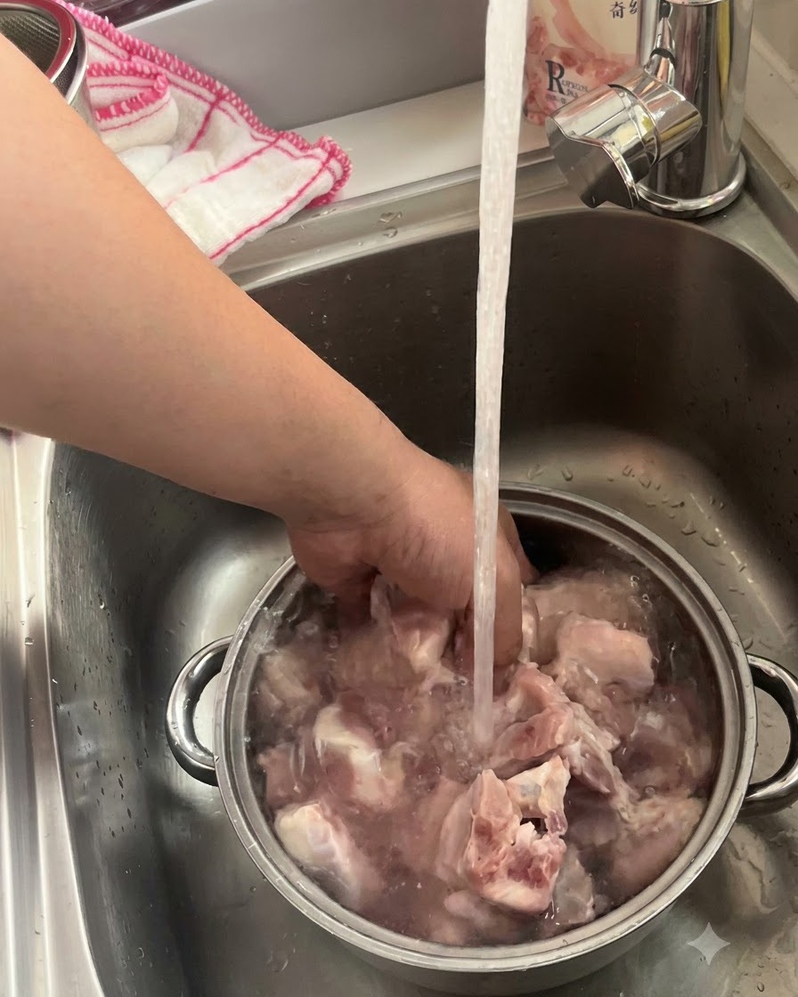 Costillas de cerdo en remojo y siendo lavadas en un tazón de metal bajo un grifo de cocina abierto.