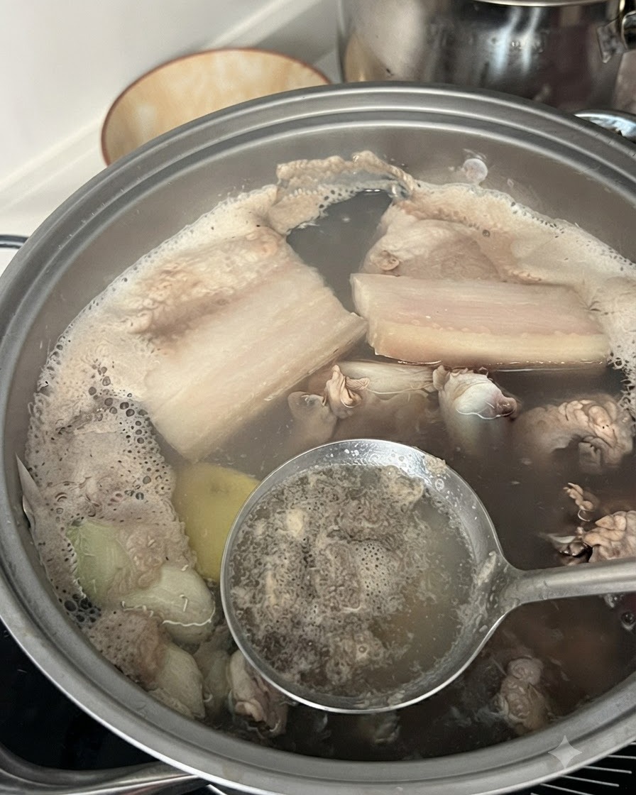 Una cuchara ranurada retirando espuma gris e impurezas del agua hirviendo en una olla que contiene costillas de cerdo.