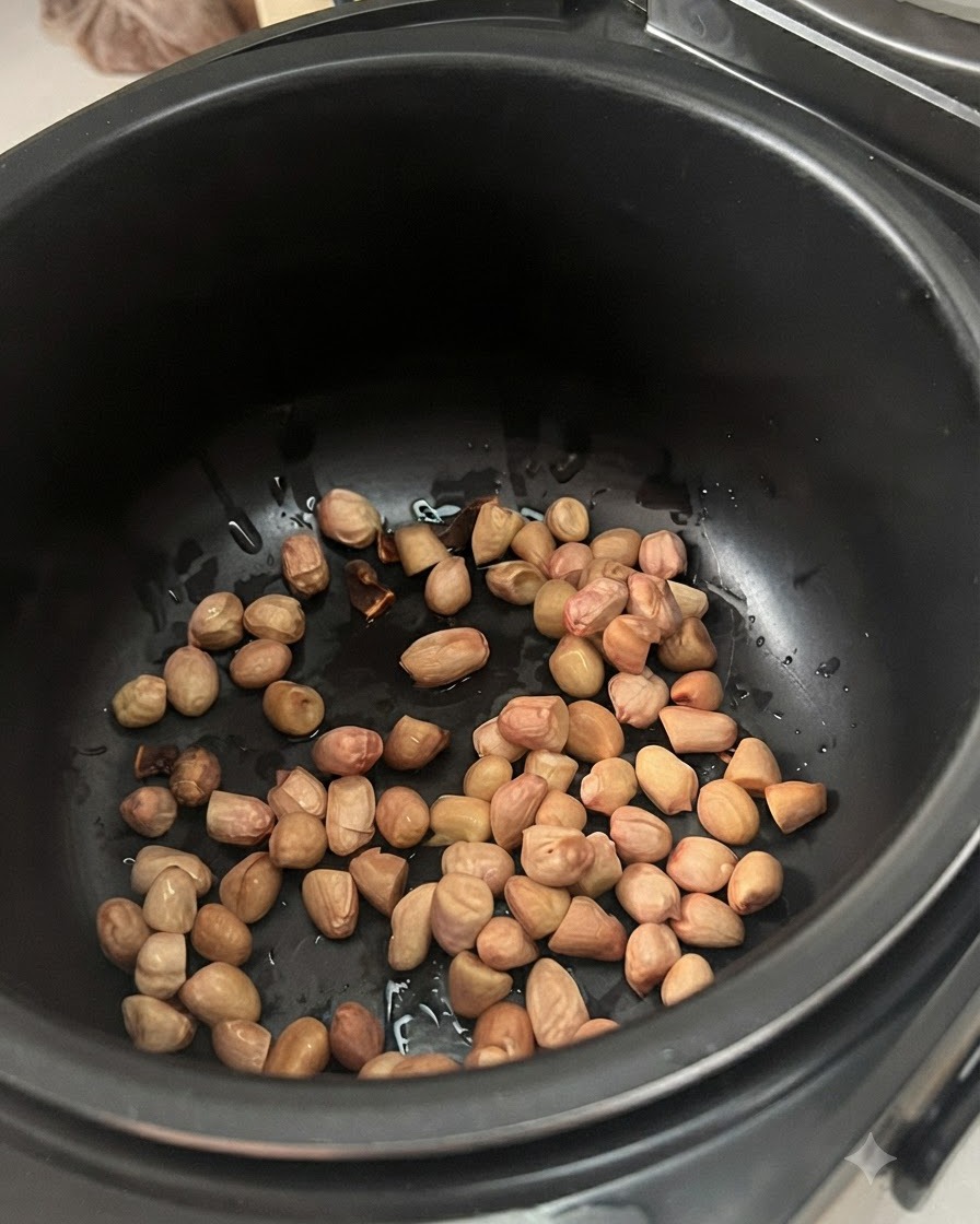 Maní remojado previamente esparcido en el fondo de una olla de cocción eléctrica oscura.