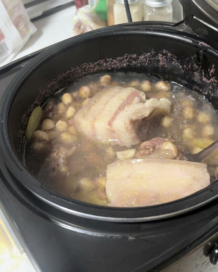 Panceta de cerdo siendo levantada y examinada con una cuchara dentro de la mezcla de caldo.