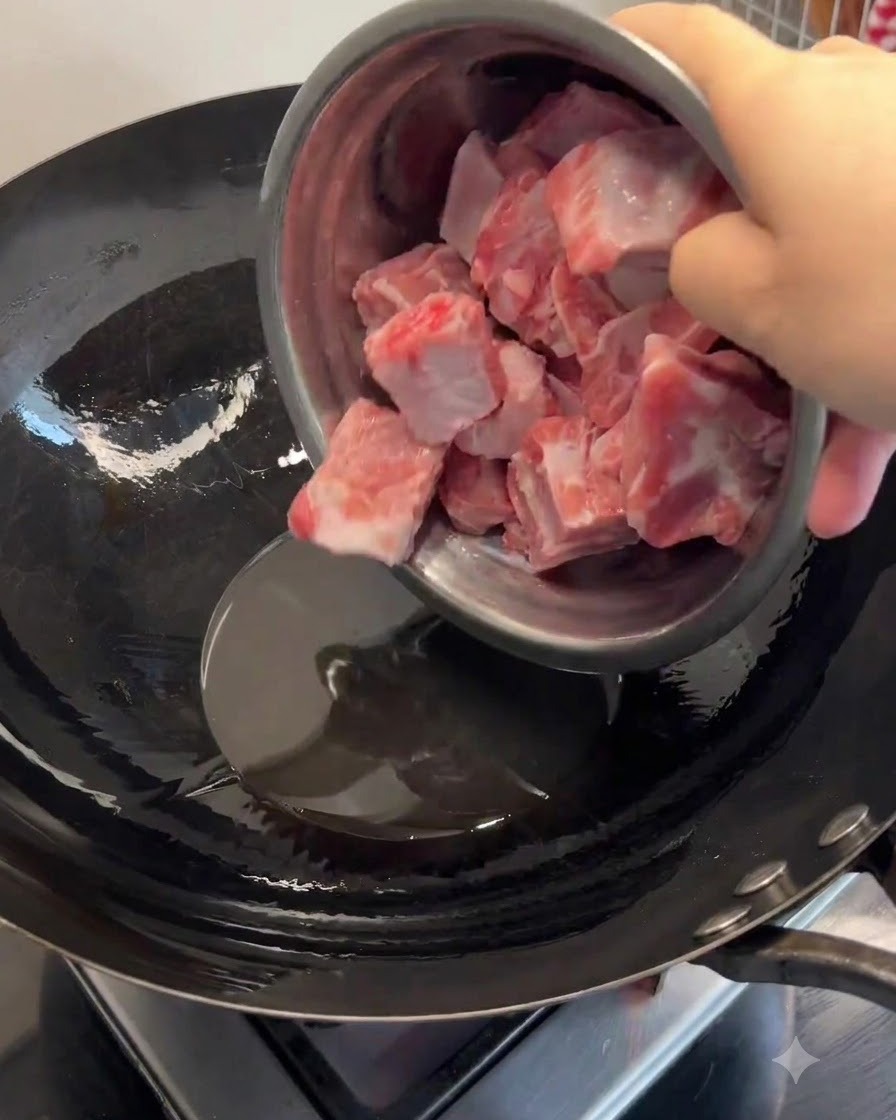 Costillas de cerdo siendo añadidas a manteca derretida en un wok caliente y fritas hasta que estén doradas.