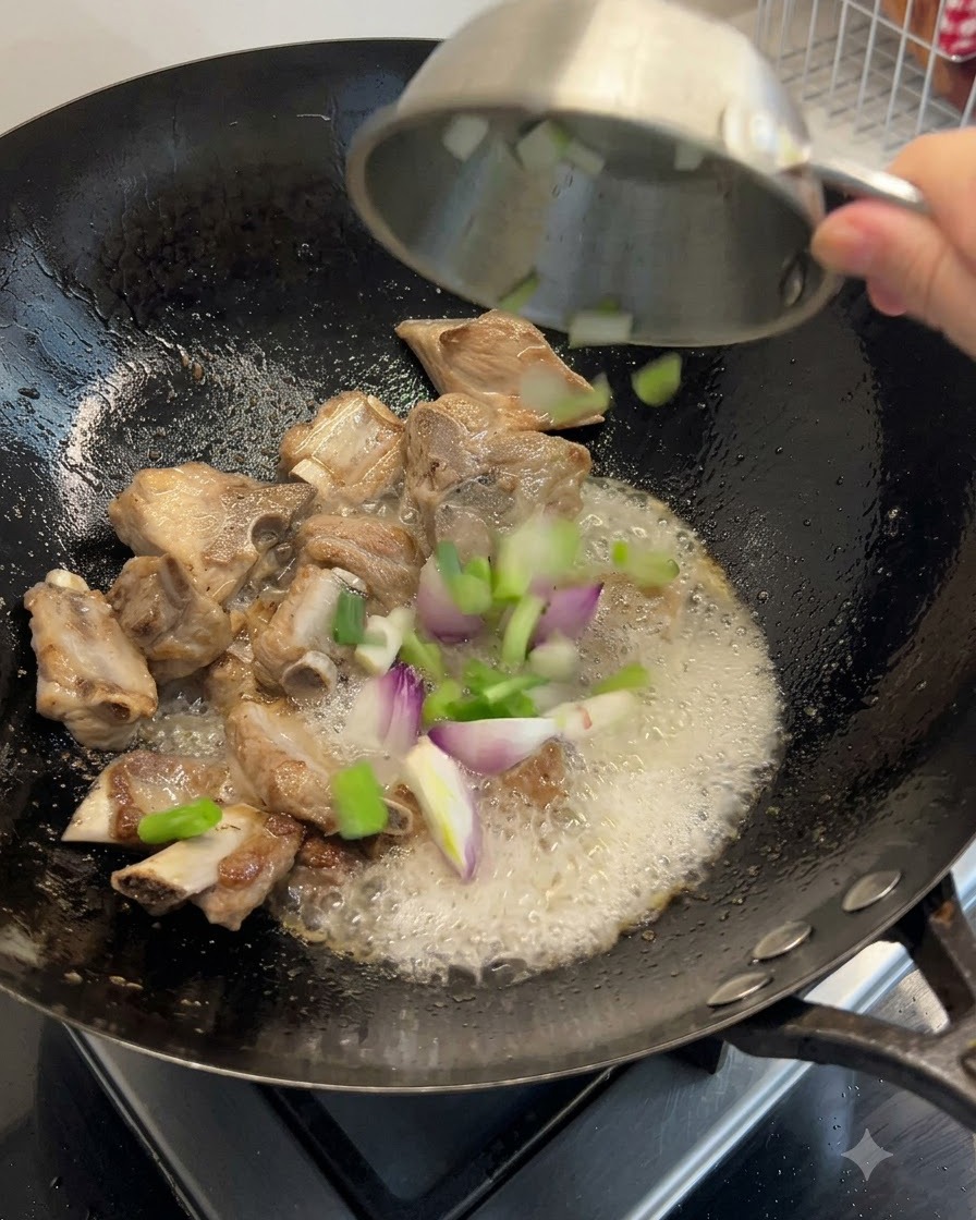 Cebolla verde, jengibre y mariscos secos siendo arrojados al wok con las costillas.