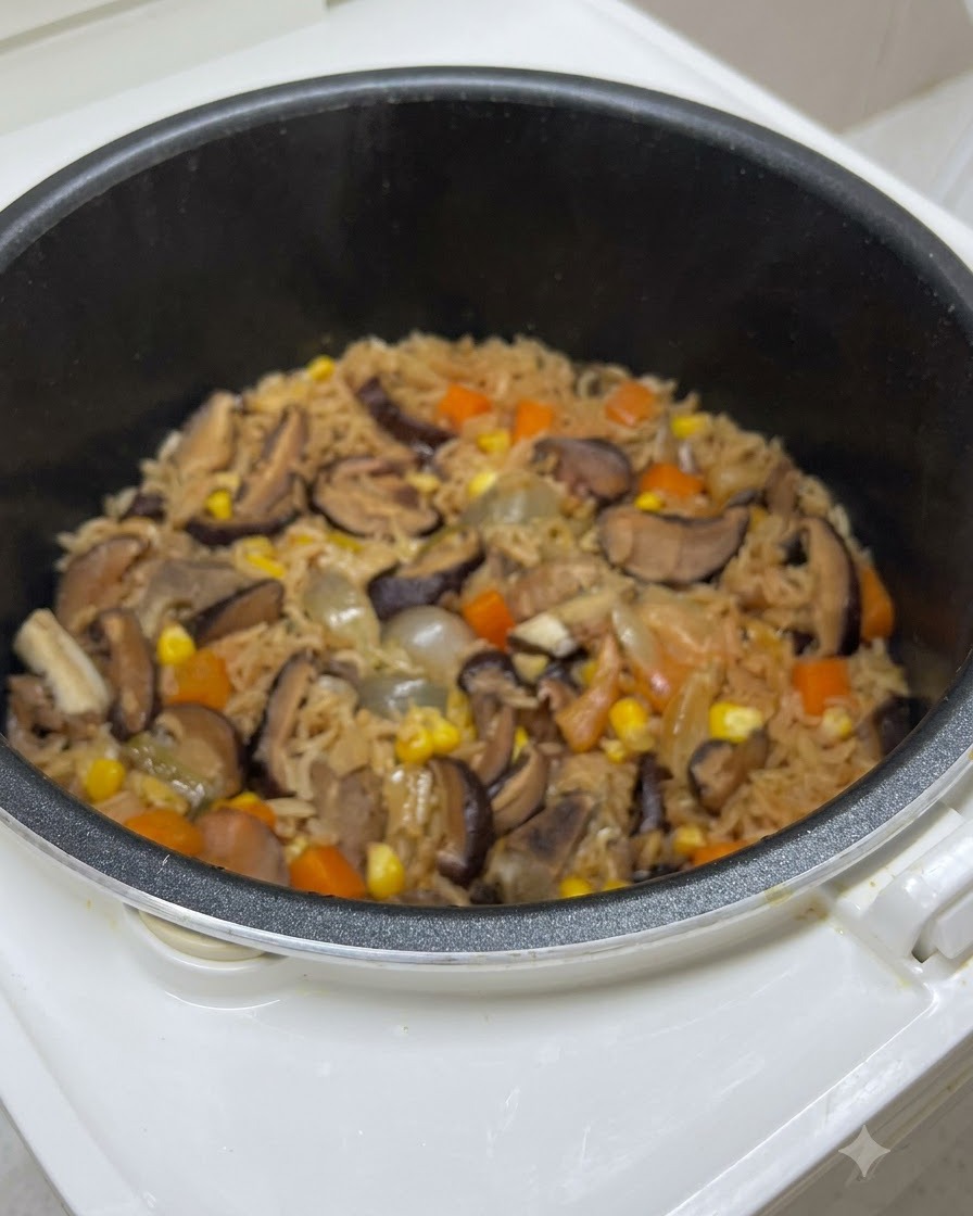 Arroz cocido mezclado con champiñones, zanahorias y maíz dentro de la olla de la arrocera justo antes de la sazón final.