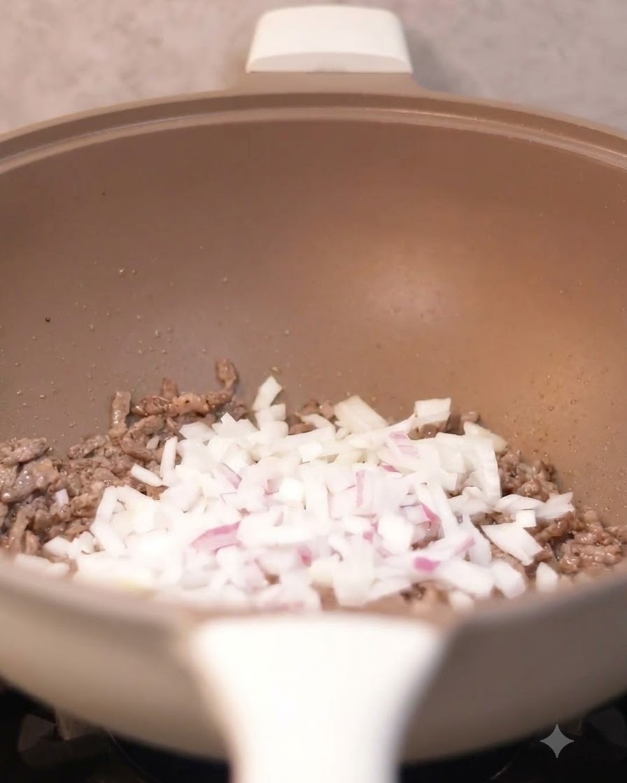 Cebollas picadas siendo vertidas en el wok con trozos de ternera cocinada.