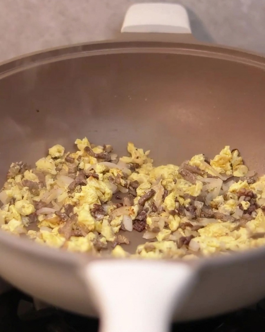 Salsa de trufa siendo añadida con una cuchara en la sartén que contiene ternera, cebollas y huevos.