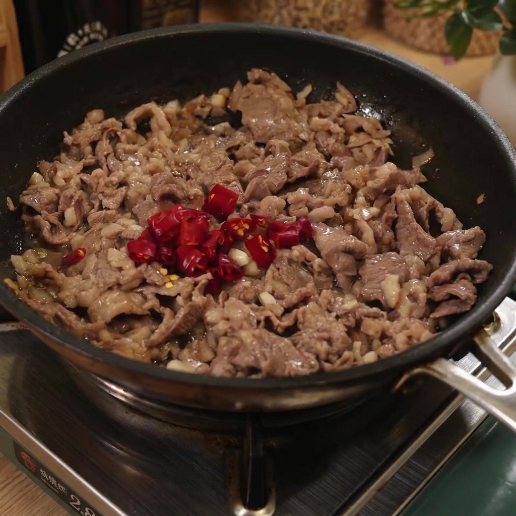 Fideos espagueti cocidos agregándose a una sartén con carne y chiles rojos en rodajas.