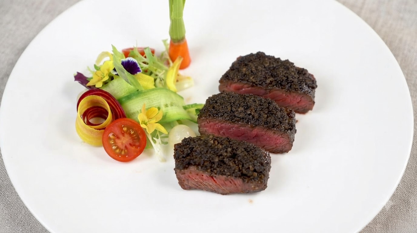 Tres gruesas rebanadas de bistec en su punto, cubiertas con rica pasta de trufa negra y servidas junto a guarniciones de vegetales frescos.