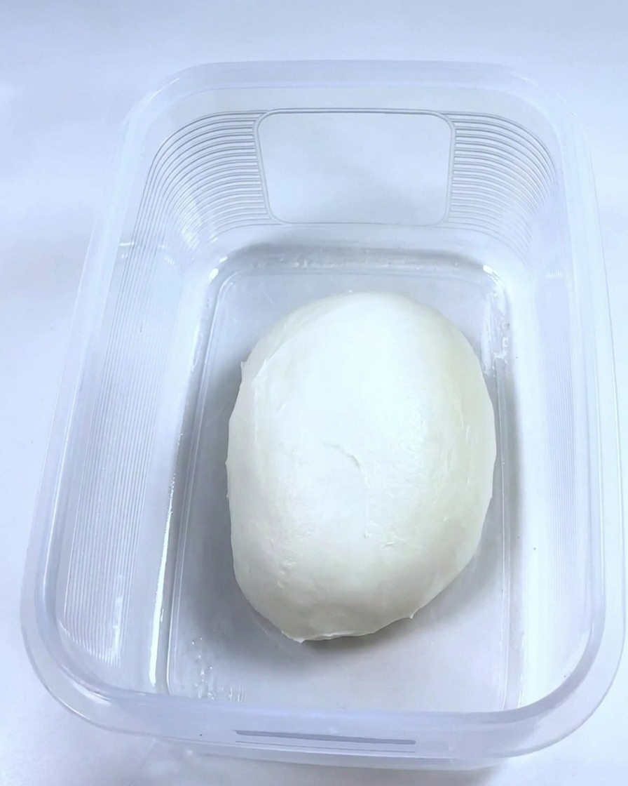 Una bola de masa suave reposando dentro de un recipiente de plástico rectangular limpio y aceitado.