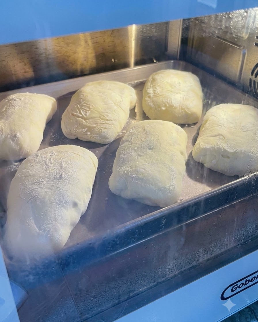Masa fermentada espolvoreada con harina sobre una bandeja de metal dentro de un horno o zona de levado.