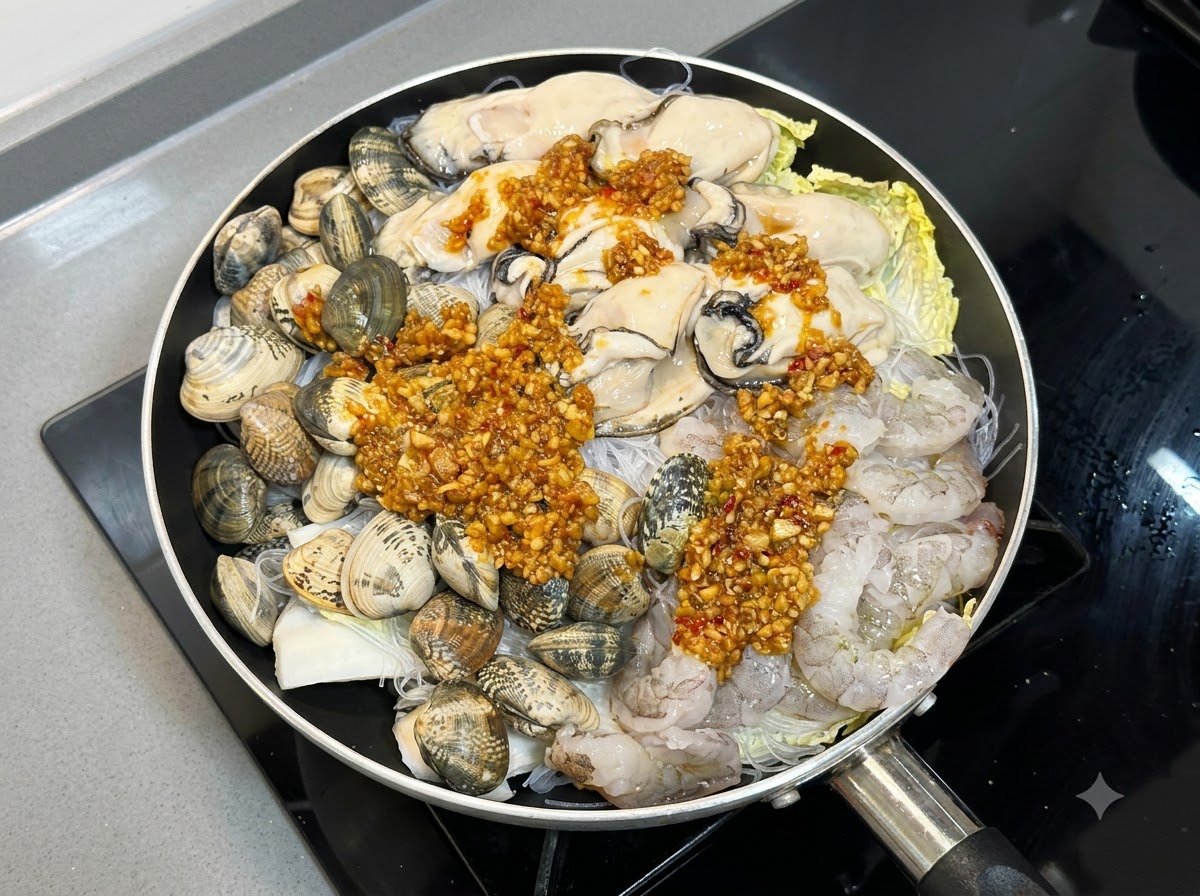 Salsa cocida de ajo y chile vertida generosamente sobre los mariscos crudos y los fideos en una sartén.