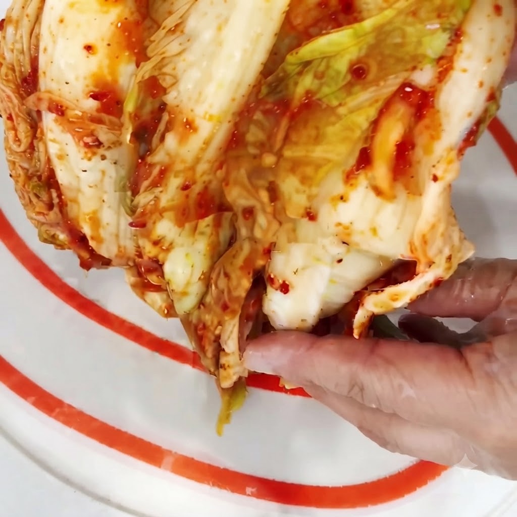 Mitad de una cabeza de kimchi siendo cortada en trozos más pequeños sobre una tabla de cortar.