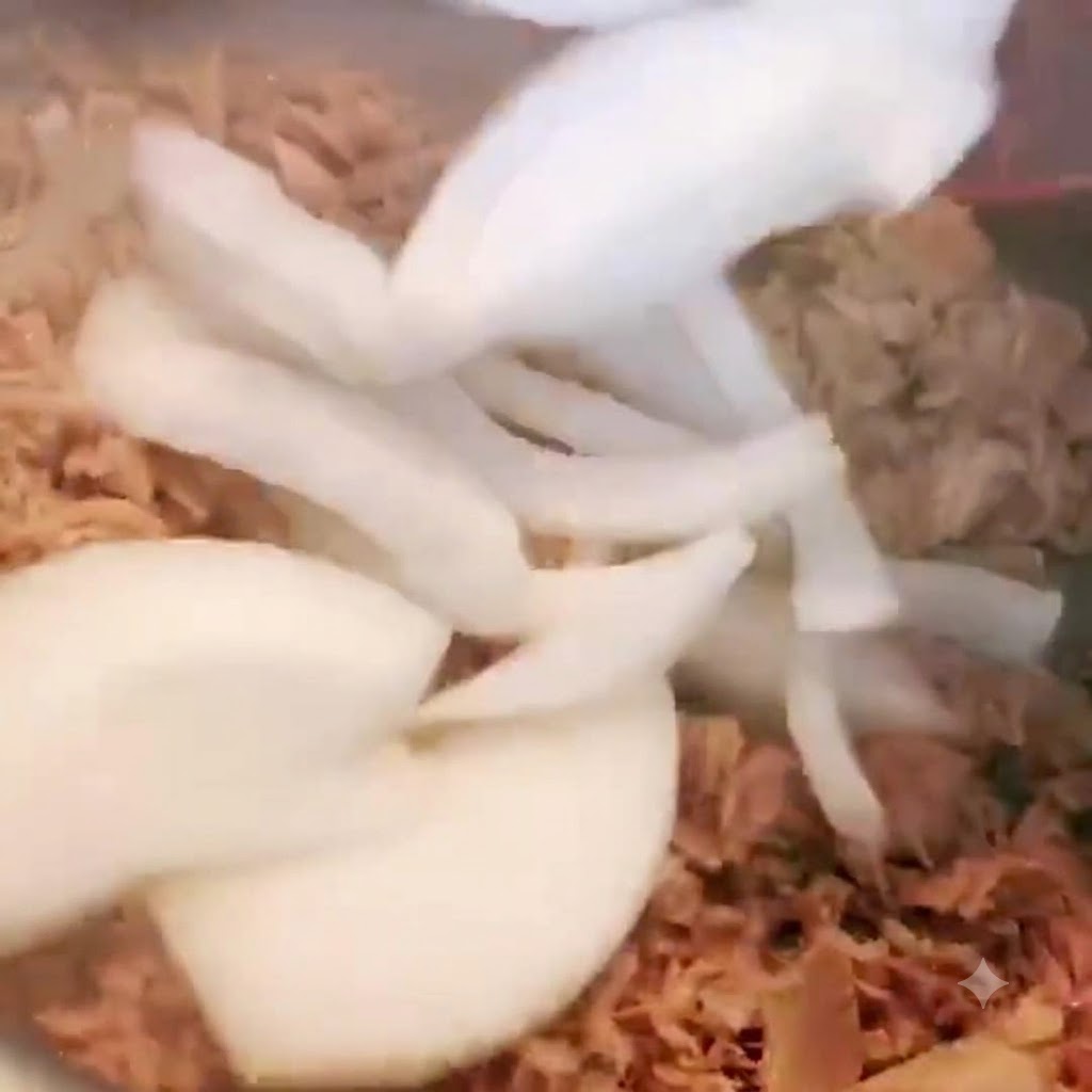 Cebollas en rodajas siendo agregadas a la olla que contiene el atún y revueltas.