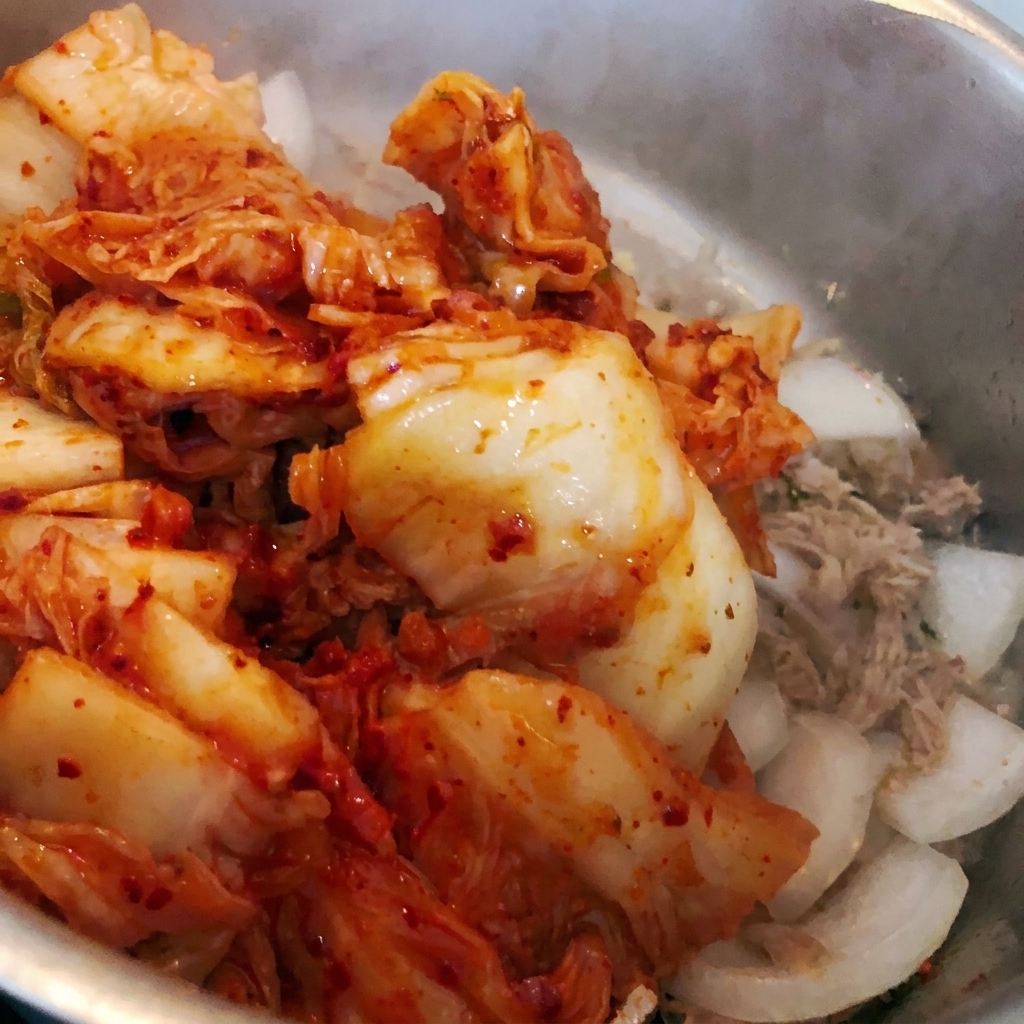 Kimchi picado siendo arrojado a la olla con los ingredientes existentes.