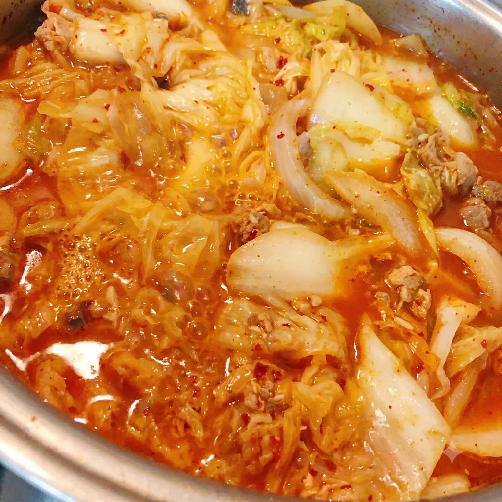 Chile en polvo siendo agregado al estofado de kimchi y atún que hierve a fuego lento.