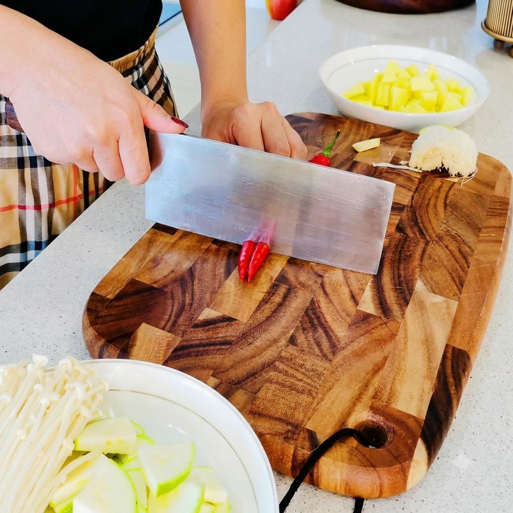 Pequeños chiles rojos siendo picados en finos trozos sobre una tabla de cortar de madera.