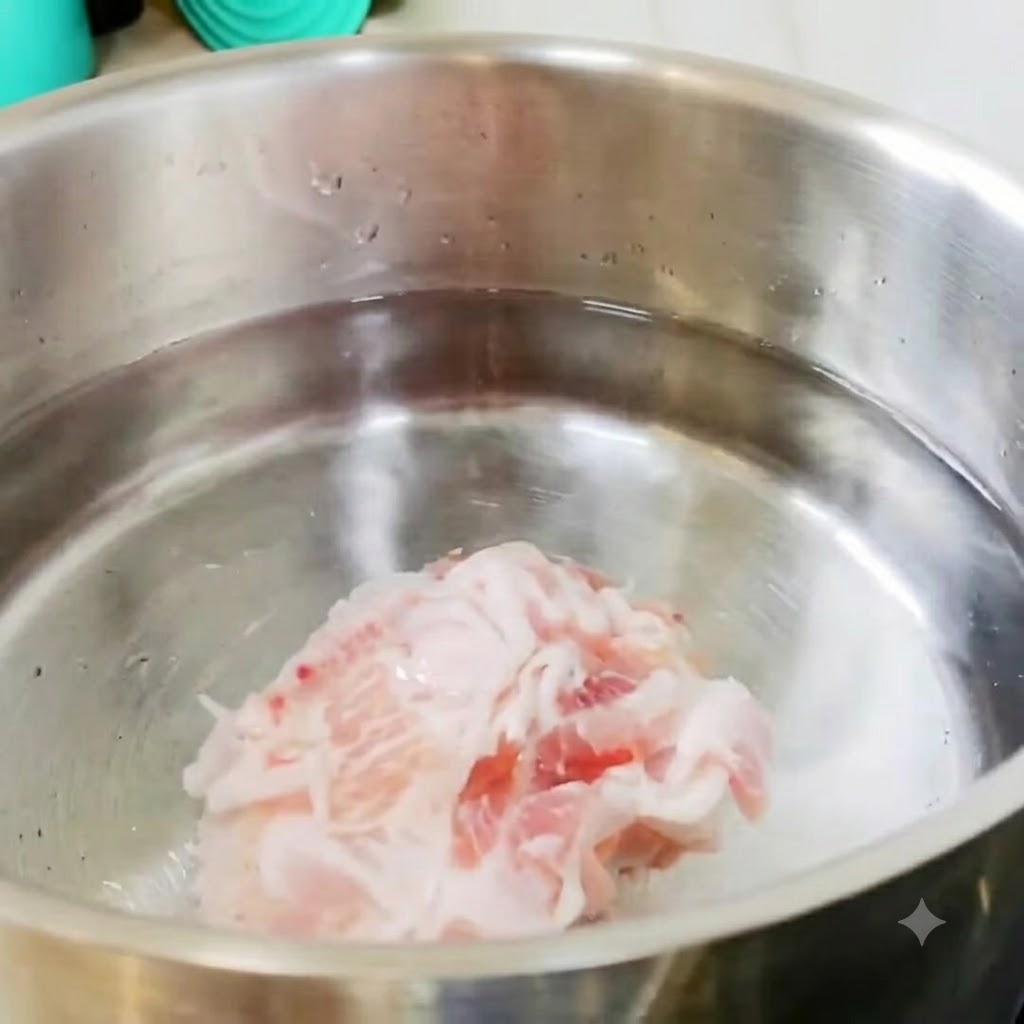 Rodajas de panceta de cerdo y trozos de patata descansando en una olla de acero inoxidable con agua fría en la estufa.