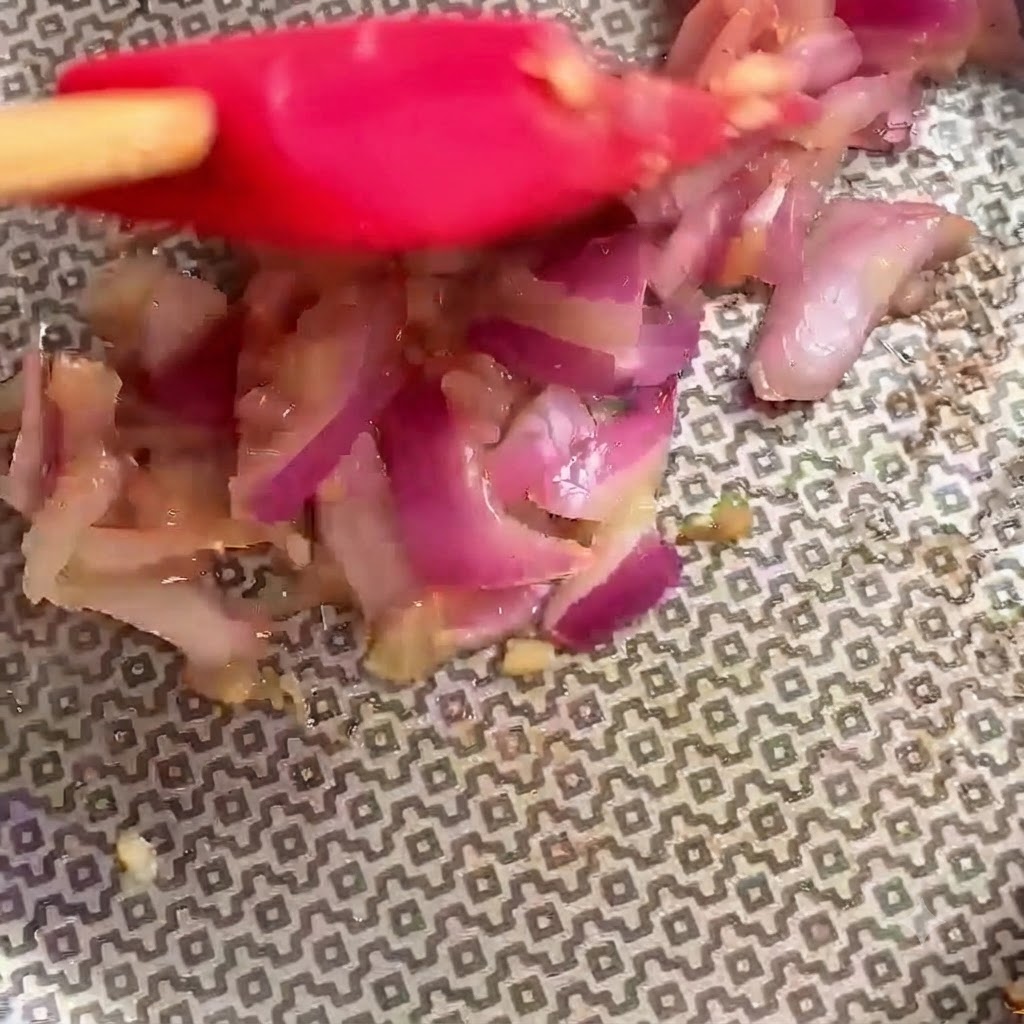 Espátula roja mezclando activamente los ingredientes dentro de la sartén.
