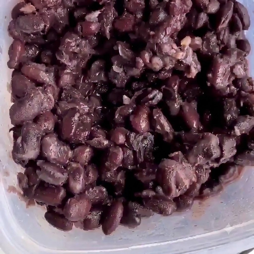 Frijoles negros cocidos dentro de un recipiente de plástico listos para machacar.