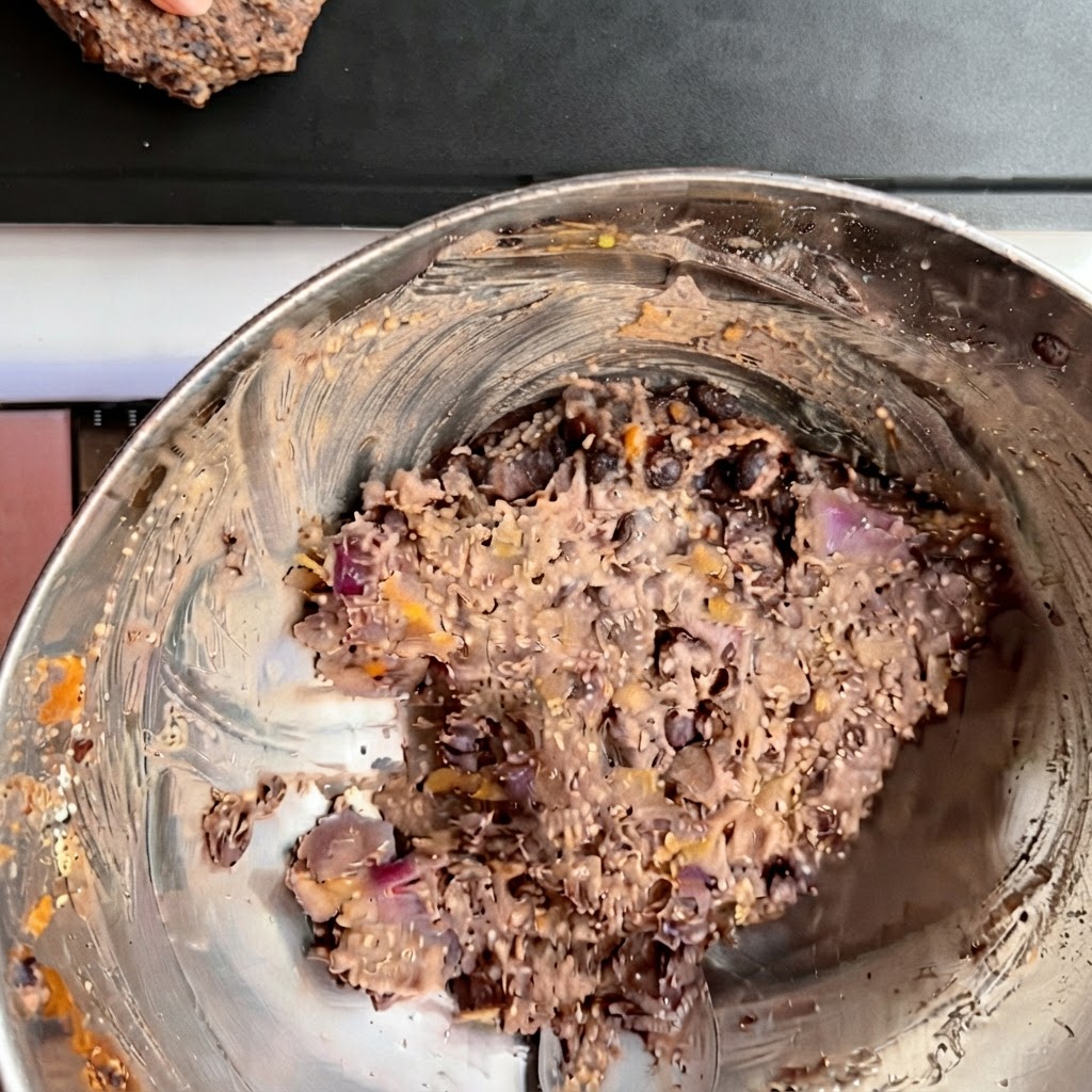 Varias hamburguesas de frijoles negros moldeadas dispuestas ordenadamente en una bandeja de horno oscura.