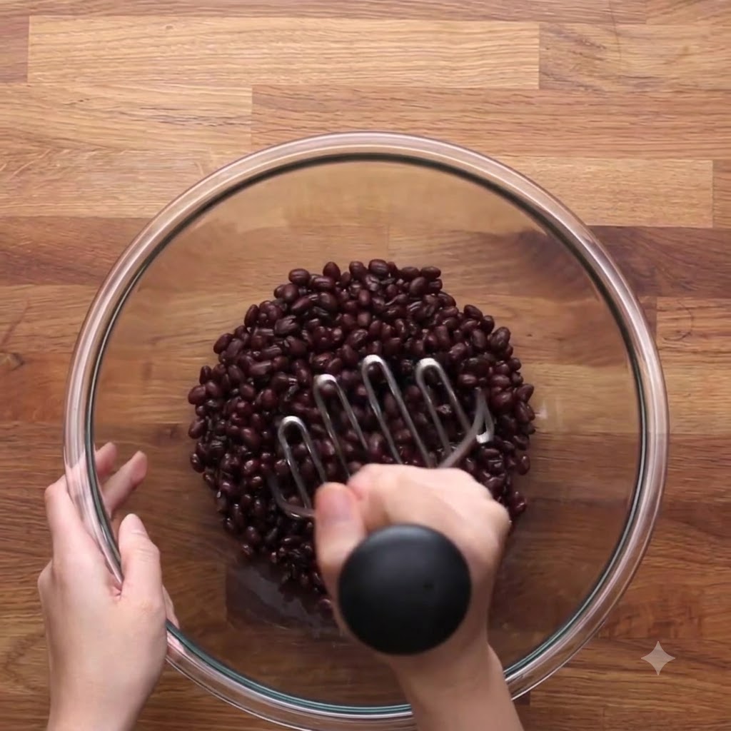 Un triturador de papas de metal presionando hacia abajo en un tazón de frijoles negros.