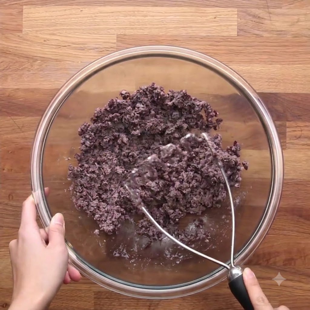 La mezcla cocida de cebolla y zanahoria combinada con los frijoles negros triturados en un tazón de vidrio.