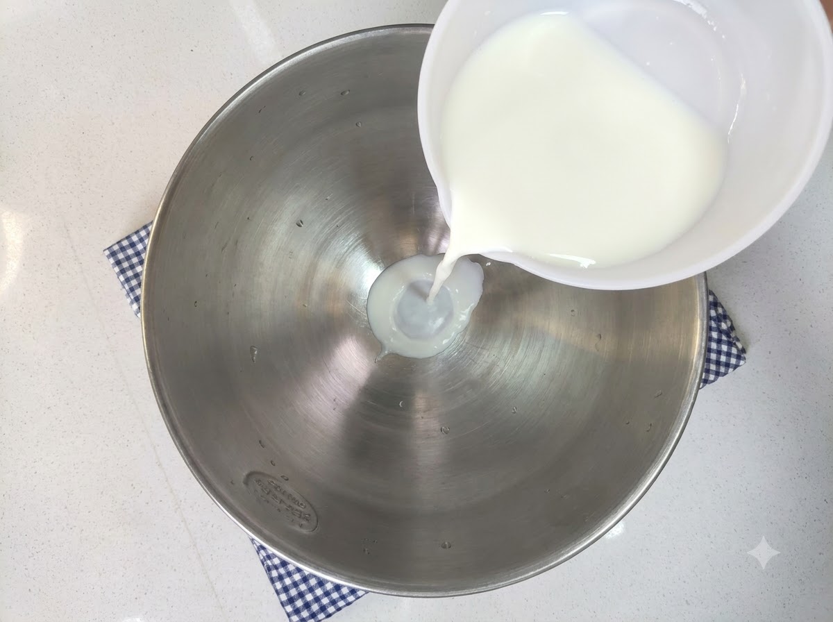 Leche, azúcar blanco, levadura, huevo y harina de alta fuerza siendo vertidos en un tazón grande para mezclar.