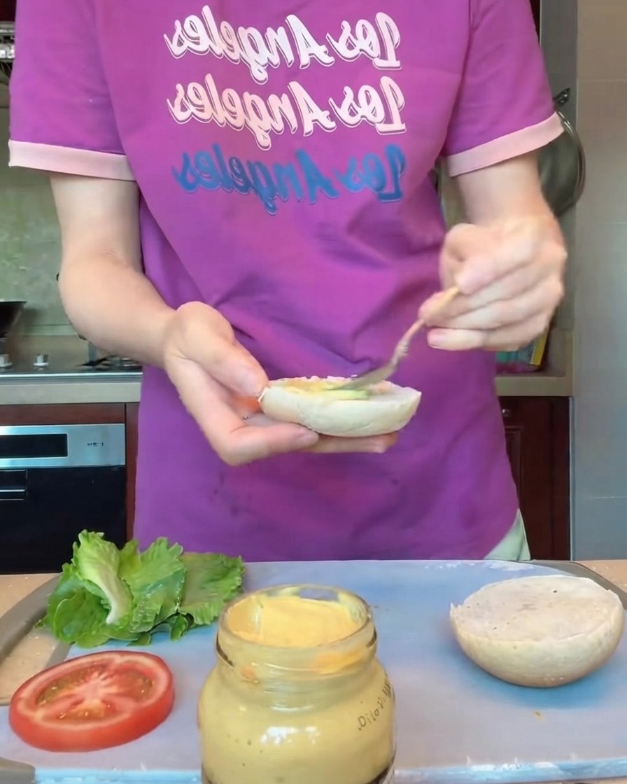 Manos usando guantes protectores dando forma a medallones de hamburguesa redondos sobre una bandeja.