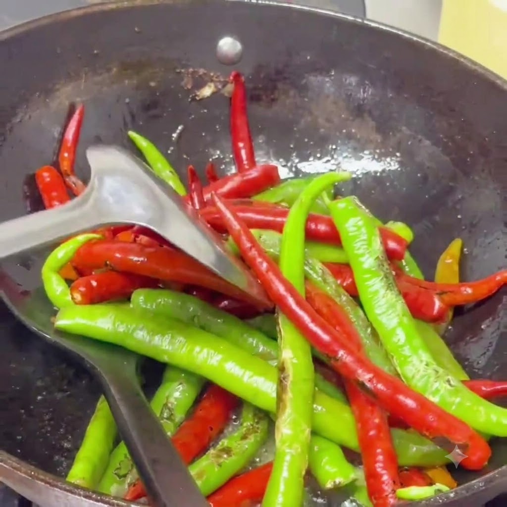 Chiles picantes ampollados siendo salteados con una espátula en un wok lleno de aceite especiado brillante.
